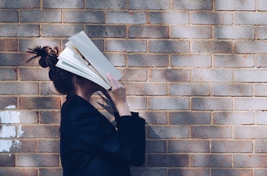 student with book on face